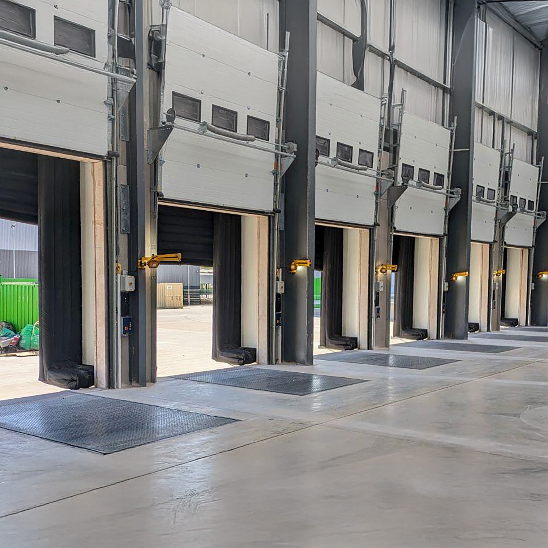 Multiple industrial garage doors with yellow swing arm dock lights in a warehouse setting.