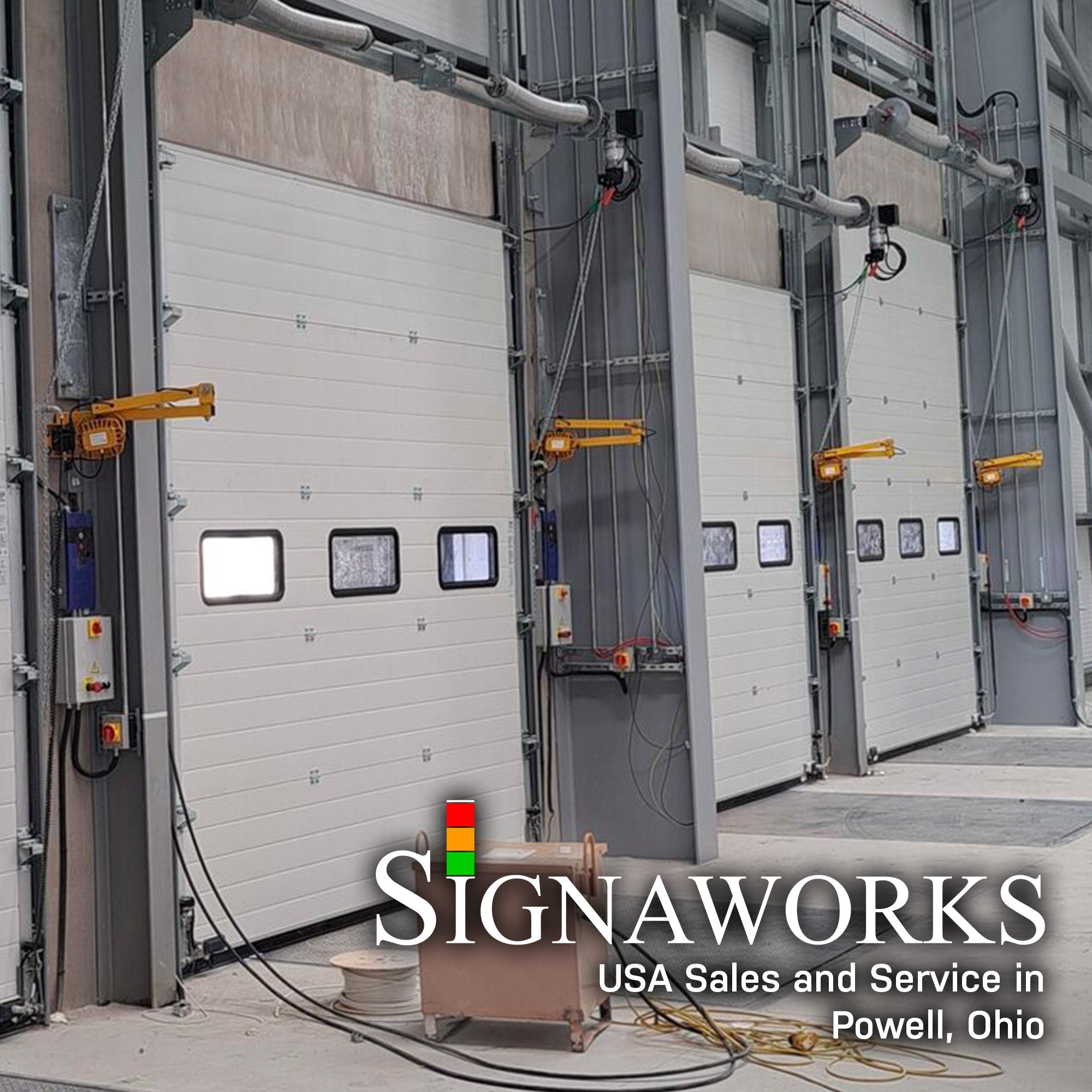 A loading dock with oversized closed garage doors and yellow industrial swing arm dock lights mounting between garage door entrances.