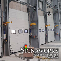 A loading dock with oversized closed garage doors and yellow industrial swing arm dock lights mounting between garage door entrances.