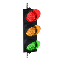 A 12 inch diameter lens LED traffic light with three lights in red, yellow, and green colors, mounted on a black housing with two steel right angle mounting brackets.
